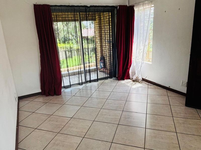 An empty living room featuring tiled flooring, sliding glass doors leading to a balcony, and natural light.