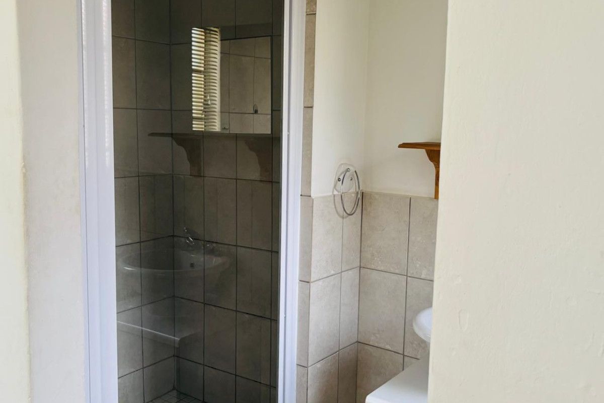 A compact bathroom featuring a tiled shower enclosure with a glass door and a small vanity basin area.