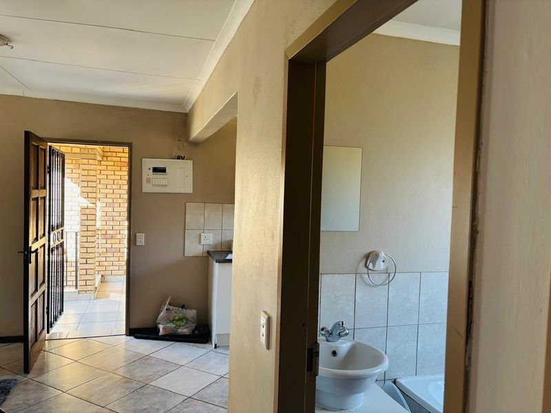 View from a hallway looking into a bathroom and kitchen area, featuring tiled flooring and basic built-in fixtures.