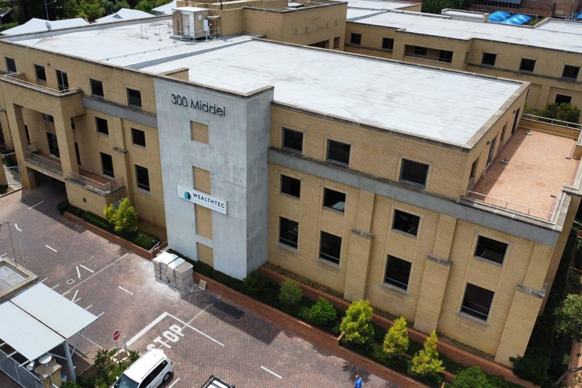 Aerial view of a multi-story commercial office building featuring brick facade, flat roofing, and paved parking area with signage.