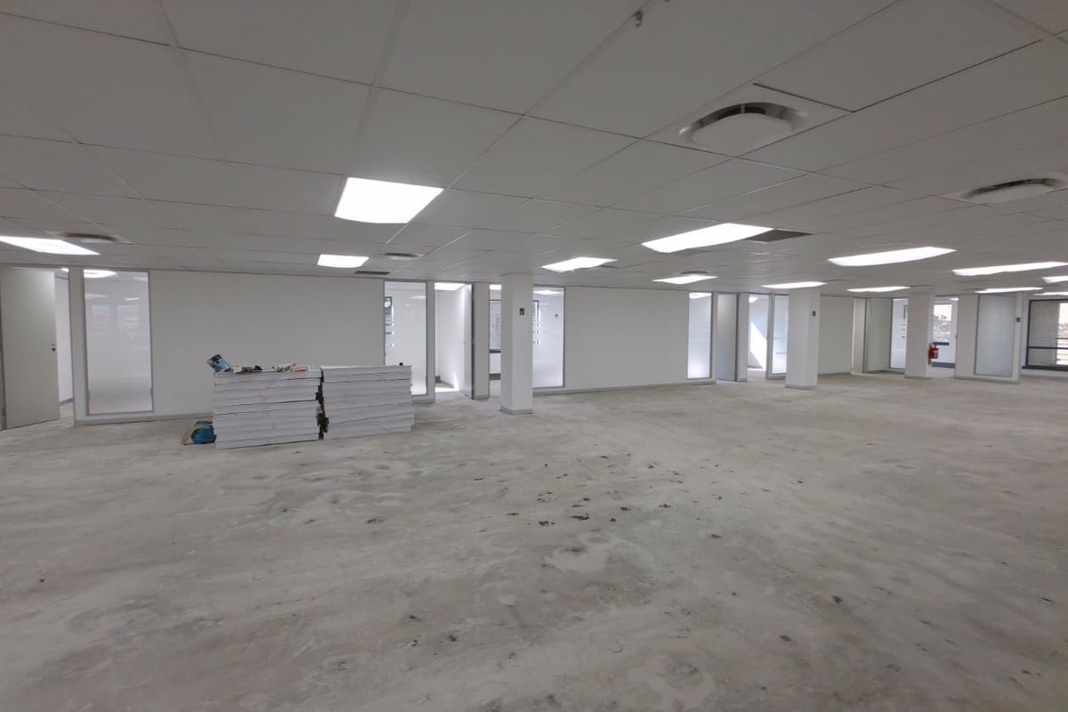 A large, open-plan commercial office space featuring a suspended ceiling with recessed lighting and glass-partitioned office rooms.