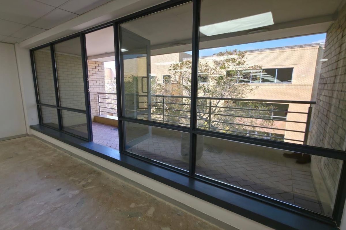 An empty commercial office space featuring large floor-to-ceiling windows and direct access to a private balcony with brick paving.