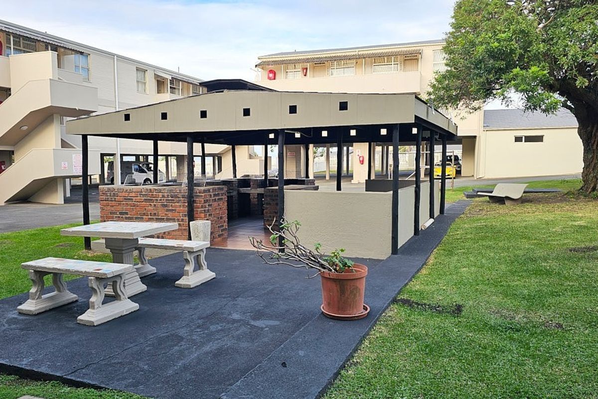 Communal outdoor entertainment area featuring a covered brick braai facility and paved seating space within the apartment complex grounds.