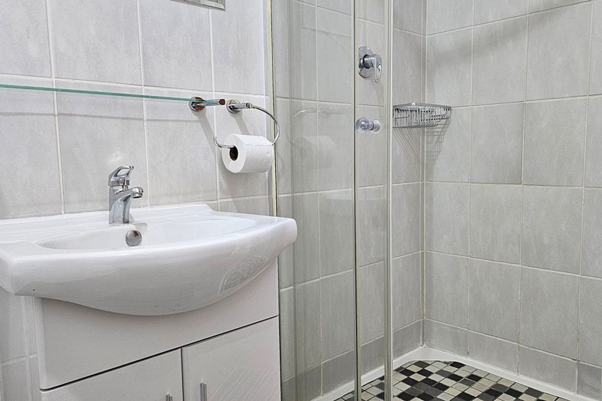 A functional bathroom featuring a white vanity with integrated basin, a glass-enclosed shower, and neutral wall tiling with a decorative mosaic floor.