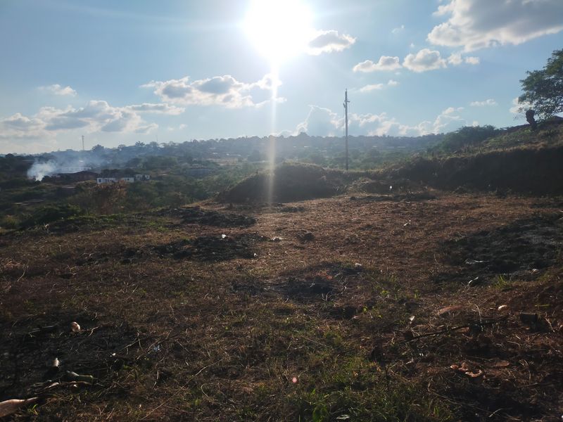An elevated view overlooking a vacant residential plot with natural landscape and distant neighborhood scenery.
