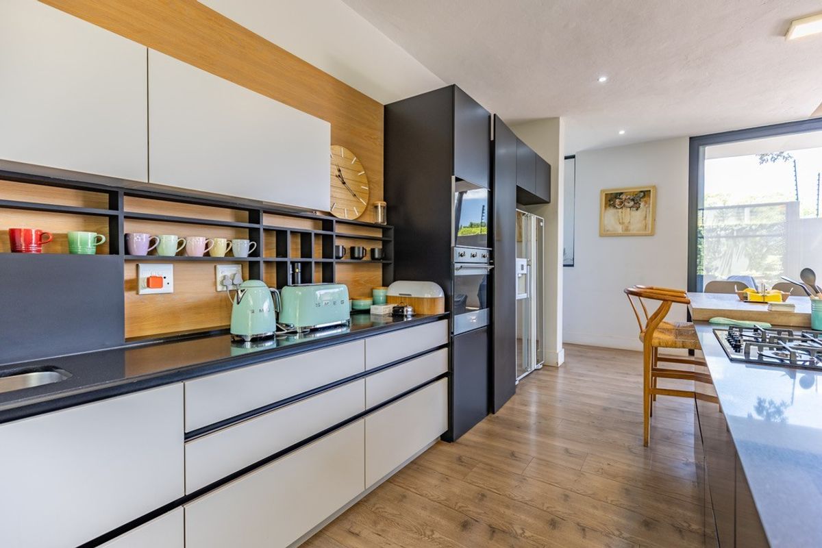 Modern kitchen featuring sleek handleless cabinetry, stone countertops, integrated oven, gas cooktop, and warm timber flooring in an open-plan layout.