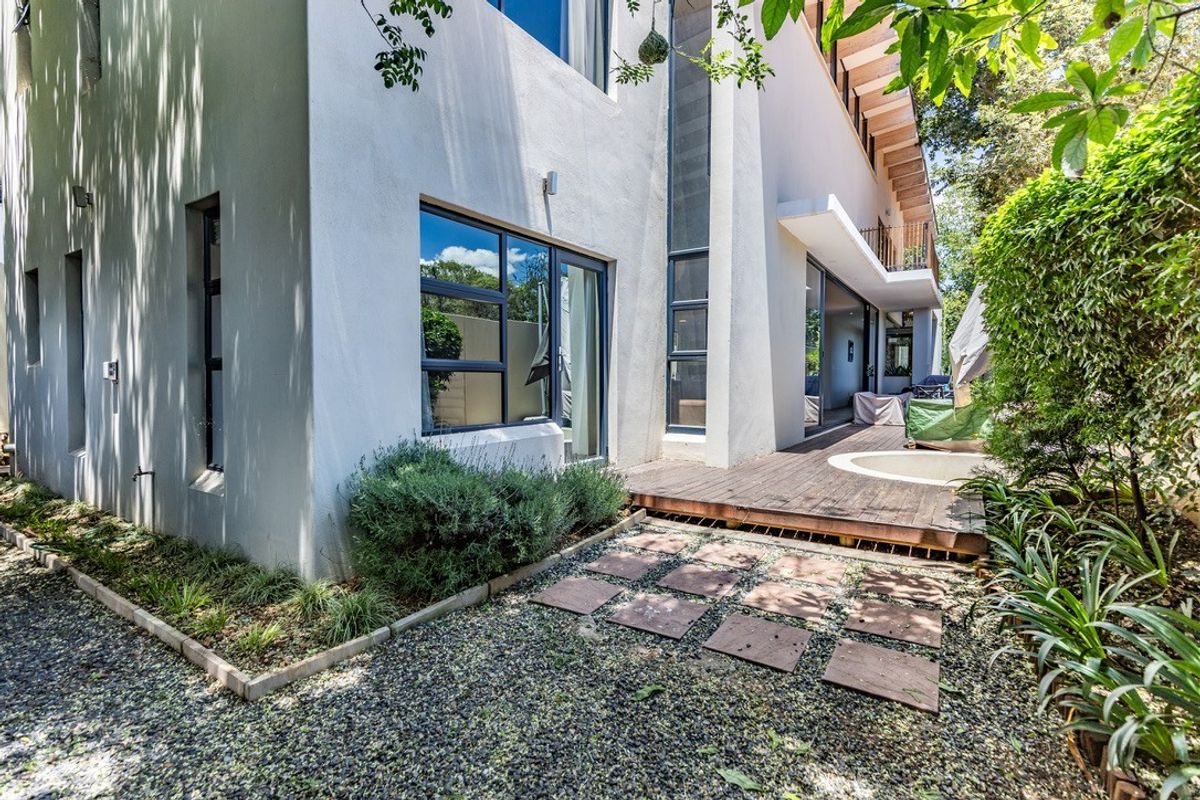 Rear exterior view featuring a modern multi-story facade, timber decking, sliding glass doors, and a landscaped garden area with gravel and pavers.