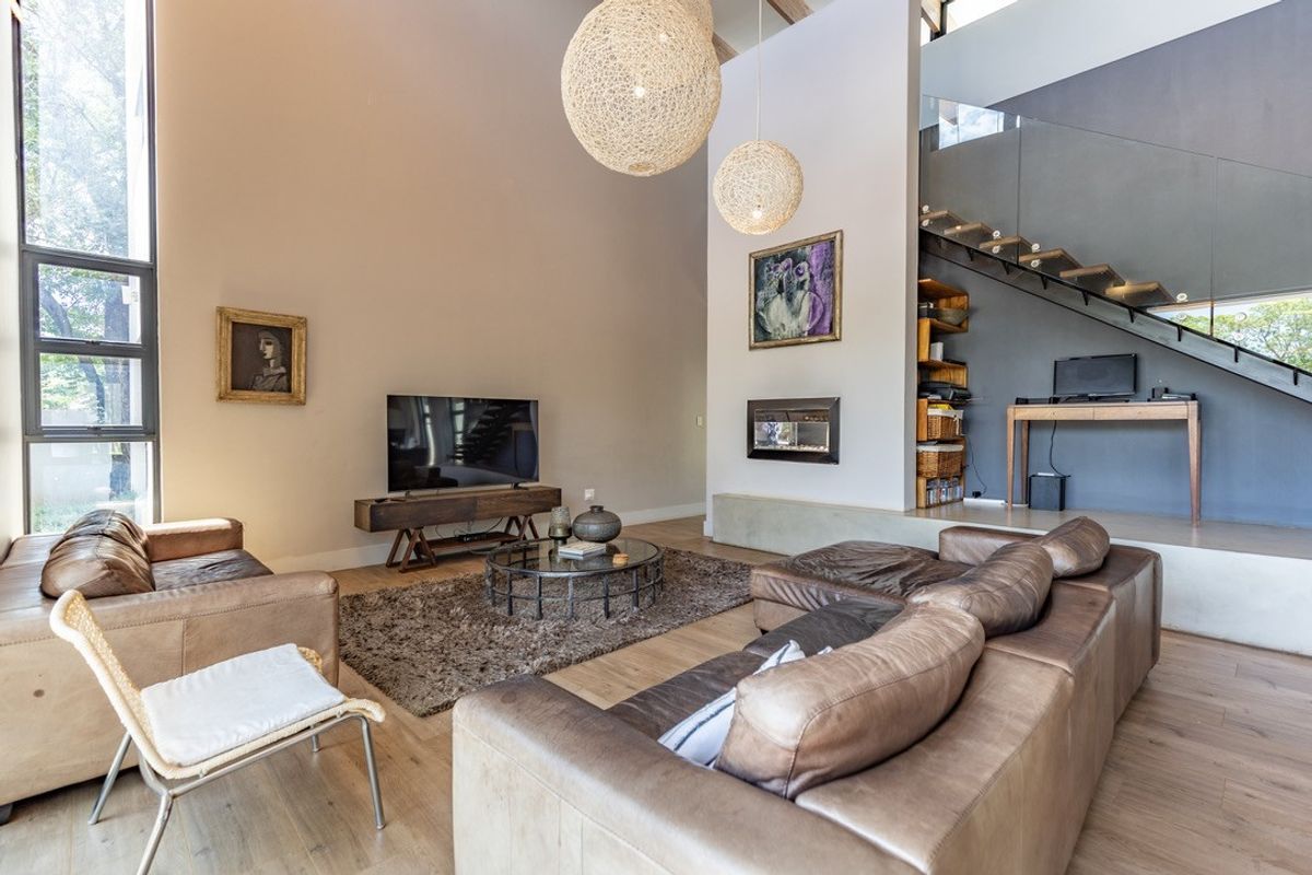 Spacious double-volume living room featuring a built-in fireplace, modern timber staircase with glass balustrade, and large windows providing ample natural light.