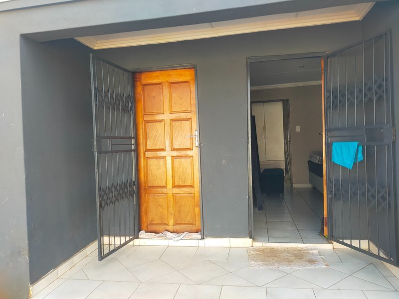 A covered patio area featuring tiled flooring and security gates, providing access to the interior of the commercial property.