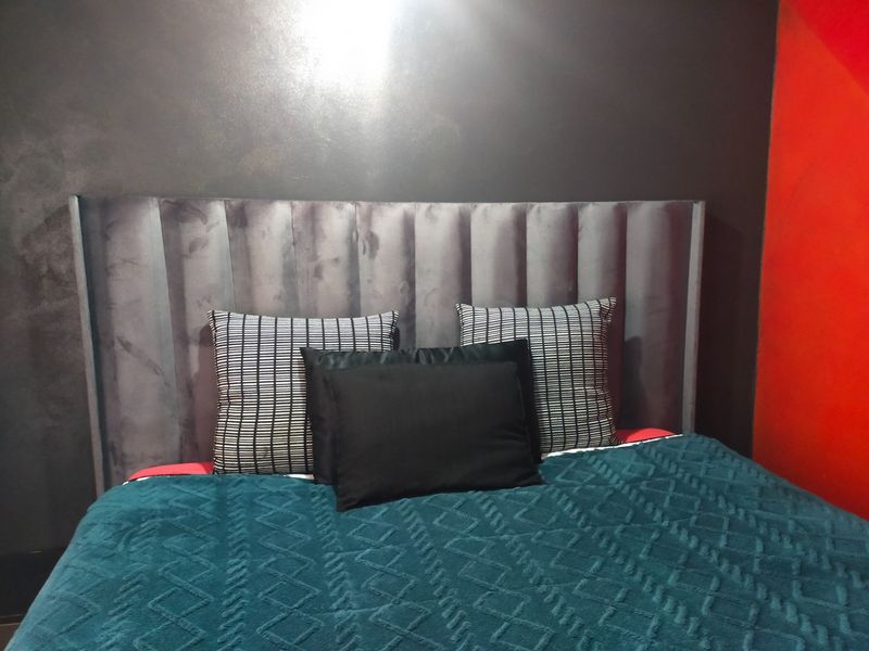 A bedroom interior featuring a dark grey upholstered headboard against a dark wall with a contrasting red accent wall.