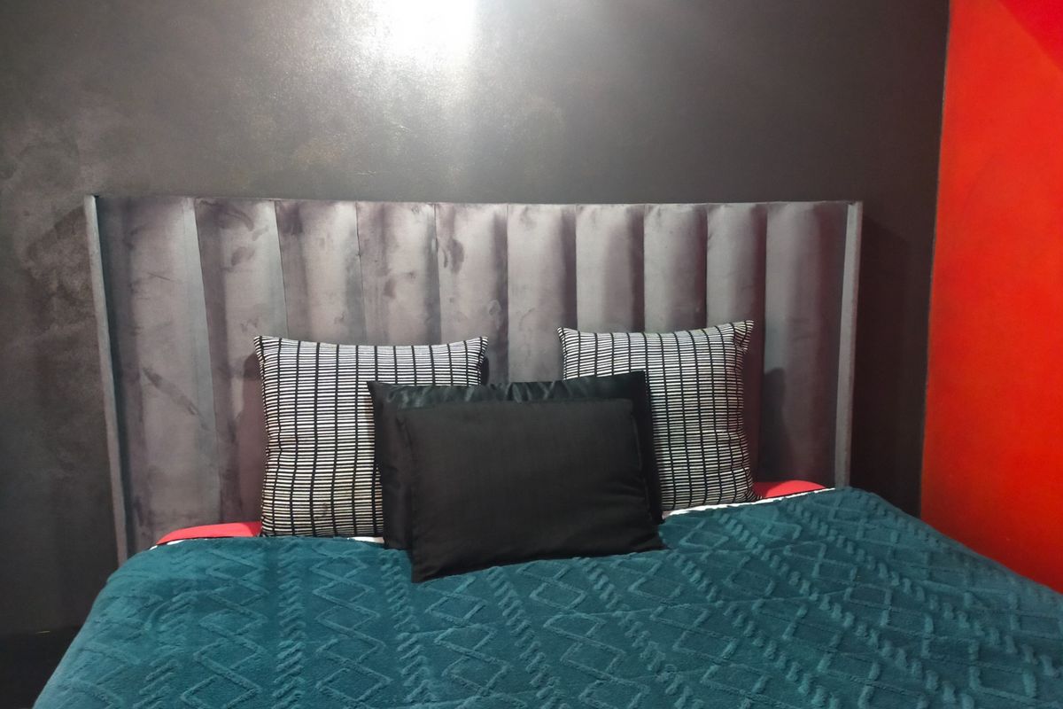 A bedroom interior featuring a dark grey upholstered headboard against a dark wall with a contrasting red accent wall.