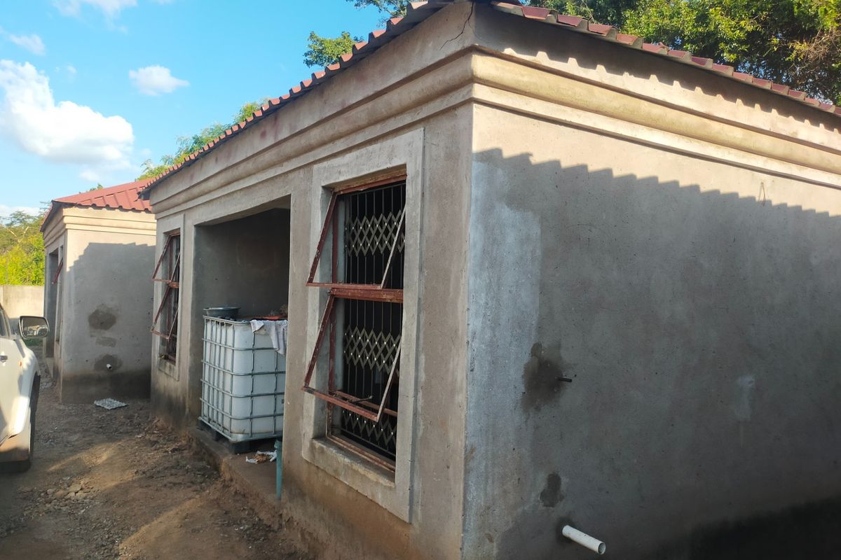 Exterior view of a commercial outbuilding featuring plastered walls, tiled roofing, and metal security window gates, showing signs of unfinished construction and weathering.