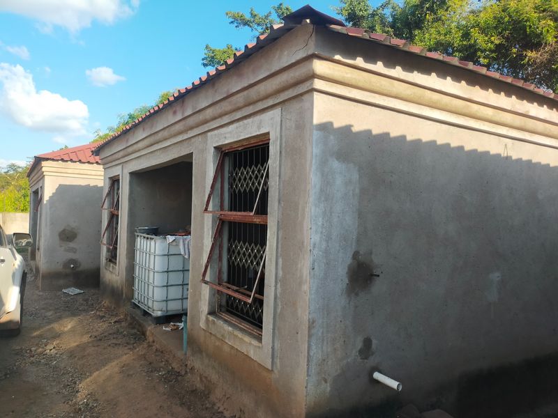 Exterior view of a commercial outbuilding featuring plastered walls, tiled roofing, and metal security window gates, showing signs of unfinished construction and weathering.