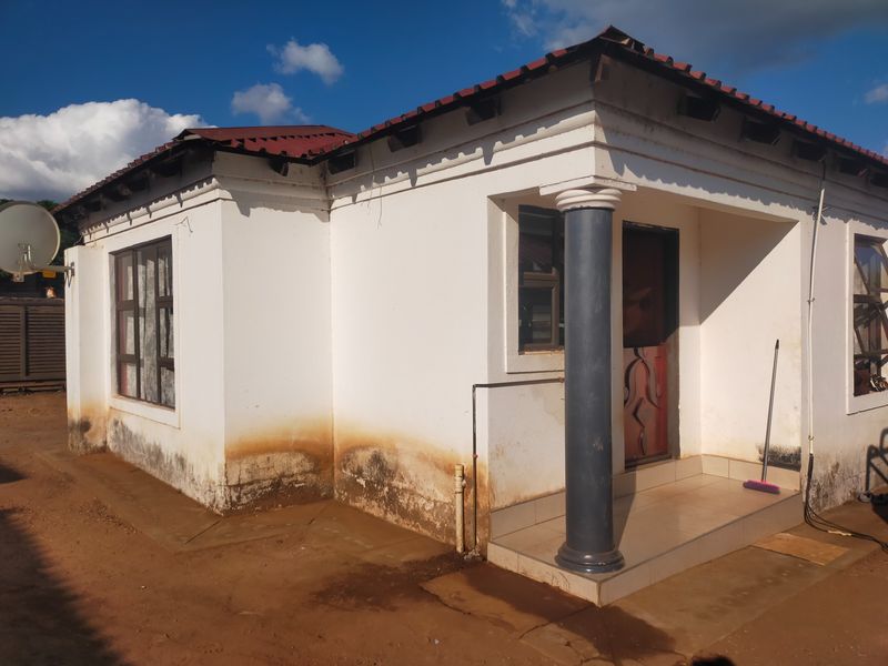 Front exterior view of a single-story commercial building featuring a tiled roof, decorative column, and entrance porch, showing signs of rising damp on exterior walls.