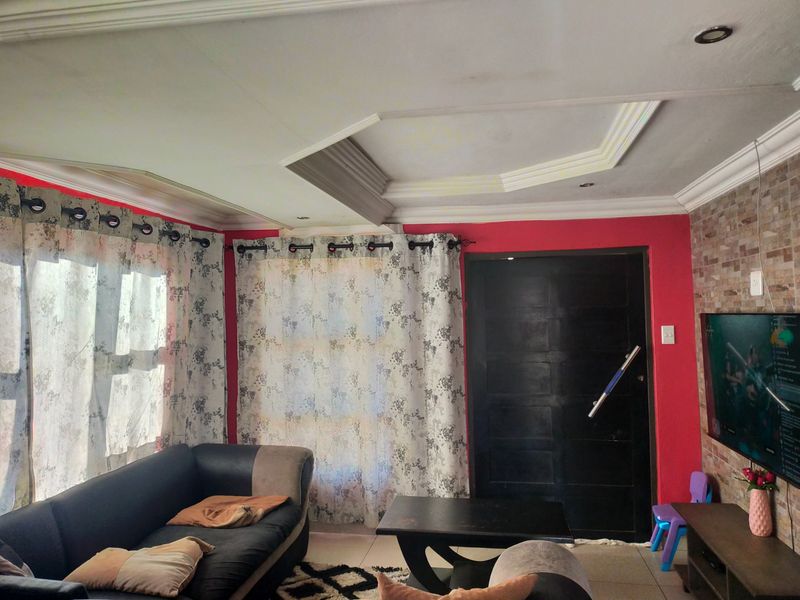 Living room featuring a stone veneer accent wall, decorative recessed ceiling with integrated lighting, and tiled flooring.