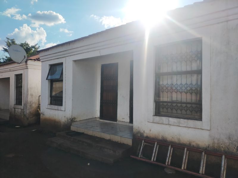 Front exterior view of a commercial building featuring a tiled entrance porch, security bars on windows, and visible wear on the exterior wall finishes.