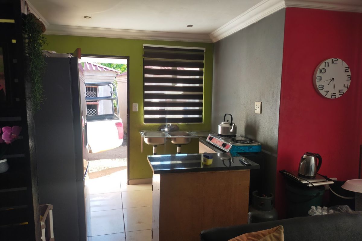 Compact kitchen area featuring a double sink, granite countertop, and direct access to the exterior, finished with tiled flooring and recessed lighting.