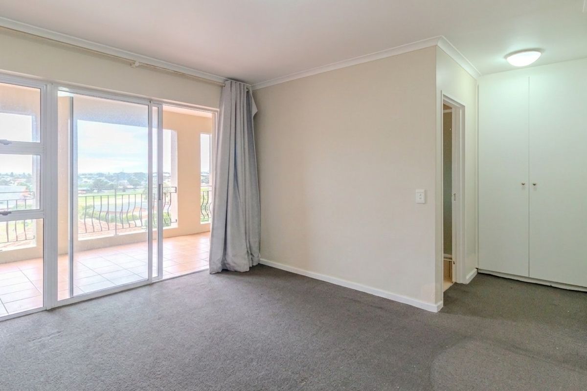 A spacious, empty bedroom featuring built-in cupboards, carpeted flooring, and a sliding glass door providing access to a private balcony.