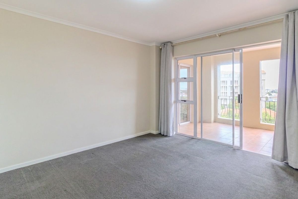 An empty living room featuring neutral walls, carpeted flooring, and a large sliding glass door providing access to an outdoor balcony area.