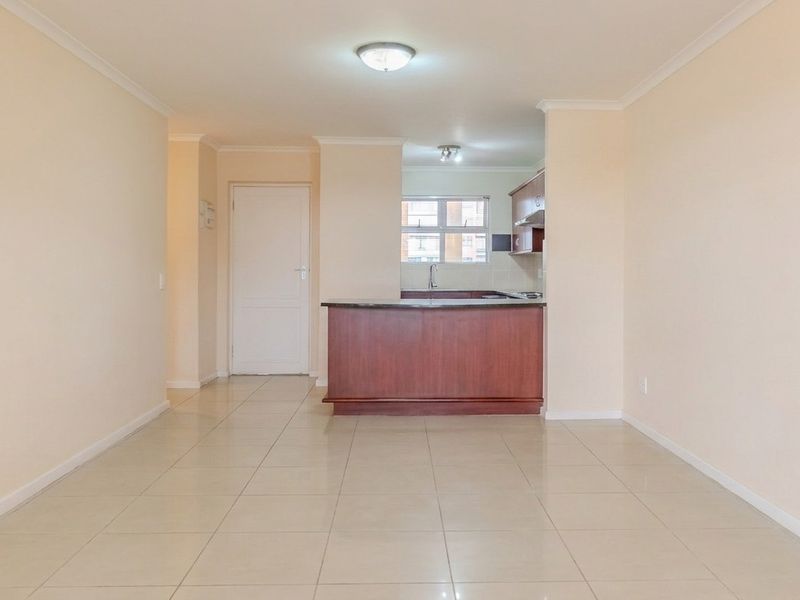 An open-plan living and kitchen area featuring neutral tiled flooring, a breakfast bar, and built-in cabinetry, offering a clean and versatile living space.