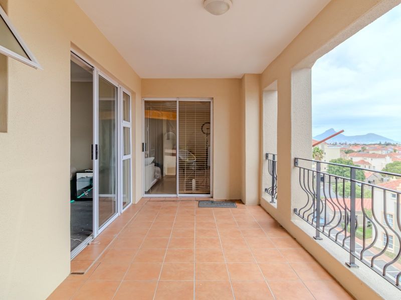 A spacious covered balcony featuring tiled flooring, metal railings, and sliding glass door access to the interior living areas.