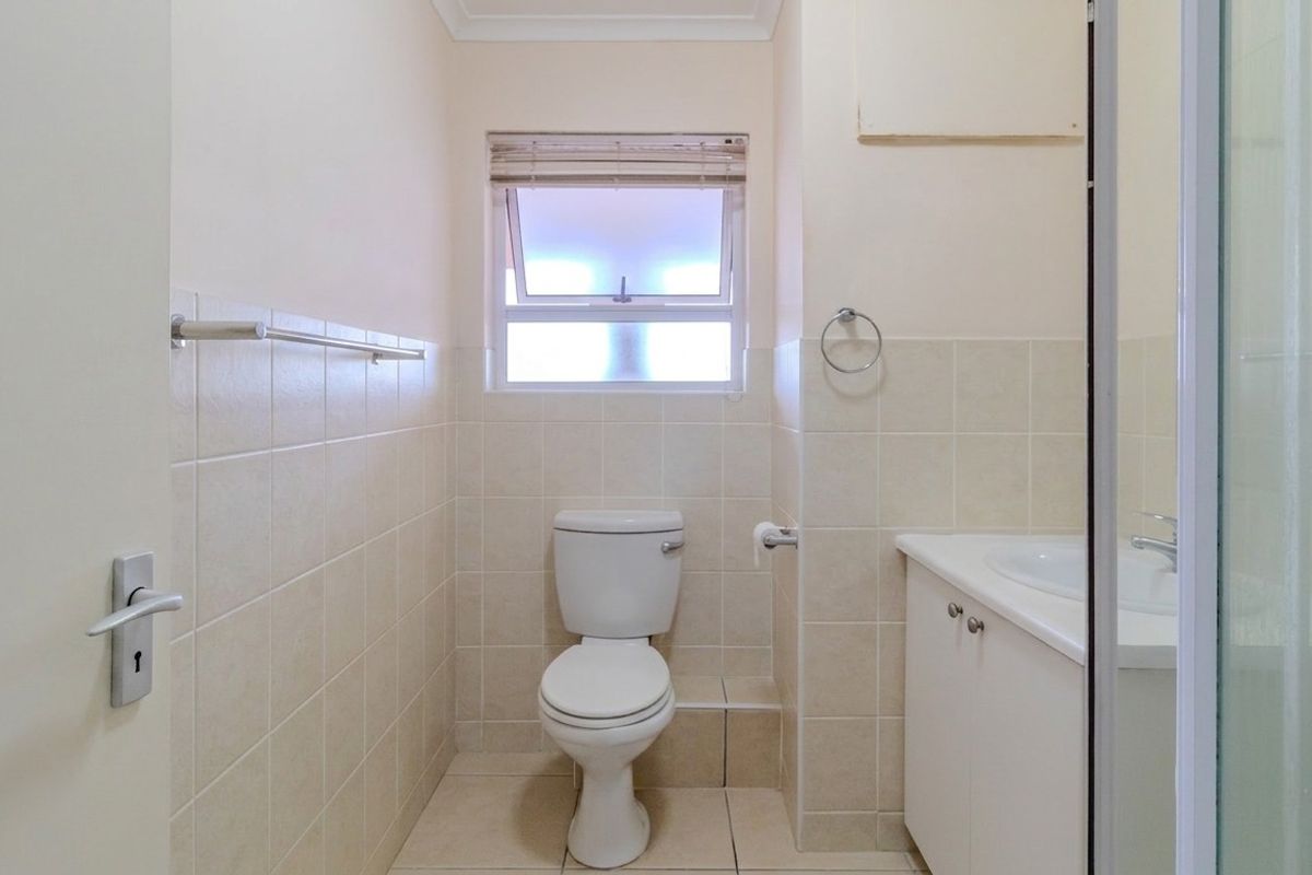 A functional bathroom featuring a toilet, vanity cabinet with integrated washbasin, tiled finishes, and a shower enclosure.