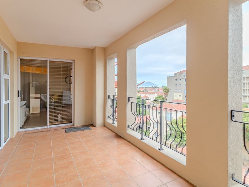 A covered balcony featuring tiled flooring, metal railings, and sliding glass door access, offering an elevated view of the surrounding neighborhood.