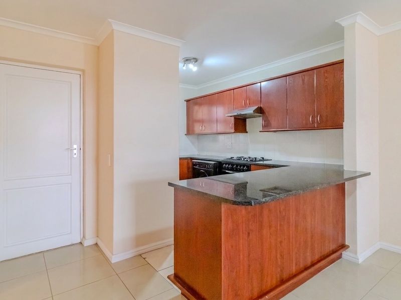A functional kitchen featuring wooden cabinetry, granite countertops, a gas hob with extractor fan, and a breakfast bar, finished with neutral tiled flooring.