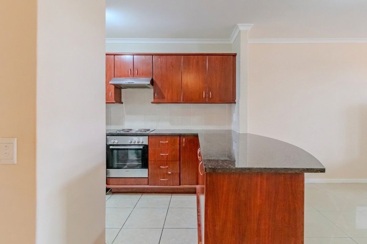 A functional kitchen featuring dark wood cabinetry, granite countertops, a breakfast bar, and built-in appliances including an oven and extractor fan.