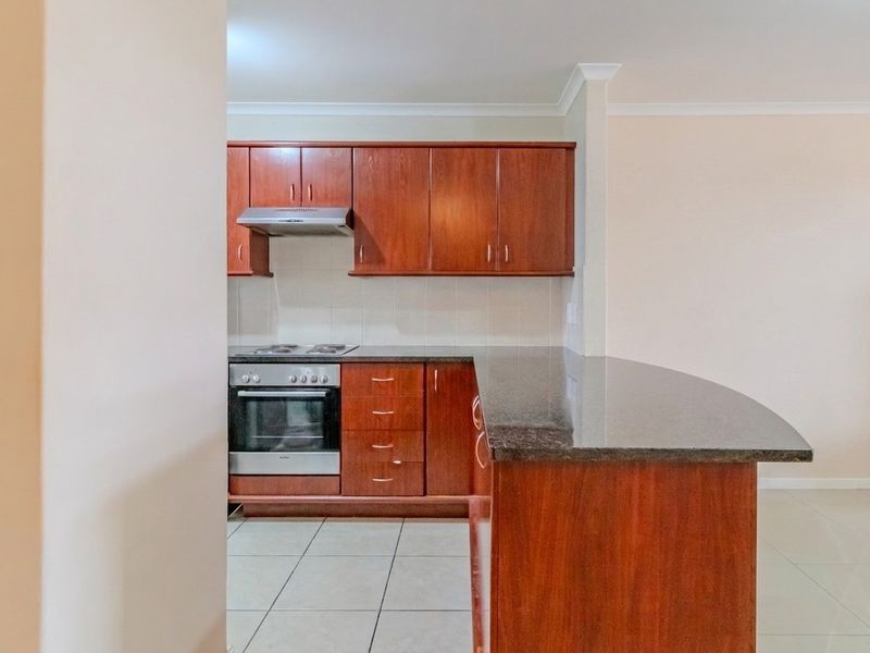 A functional kitchen featuring dark wood cabinetry, granite countertops, a breakfast bar, and built-in appliances including an oven and extractor fan.