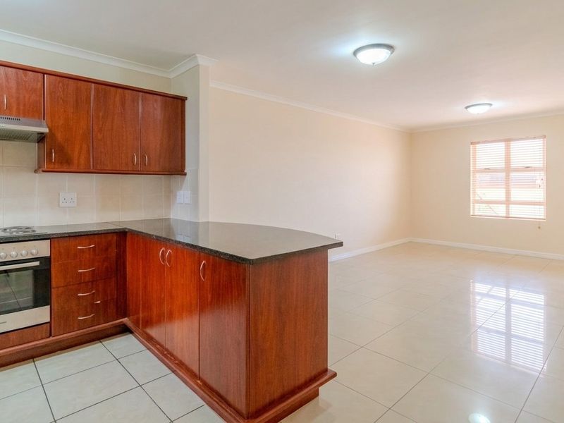 Open-plan kitchen and living area featuring wood-finish cabinetry, granite countertops, built-in oven and hob, and neutral tiled flooring throughout.
