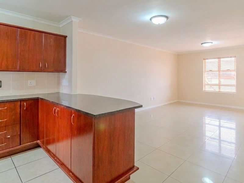 Spacious open-plan living area featuring a functional kitchen with wood-finish cabinetry, granite countertops, and integrated oven, flowing into a bright, tiled living space.