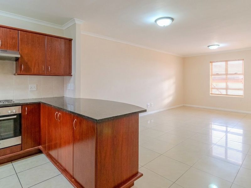 Spacious open-plan living area featuring a functional kitchen with wooden cabinetry, granite countertops, and integrated appliances, finished with neutral tiled flooring throughout.