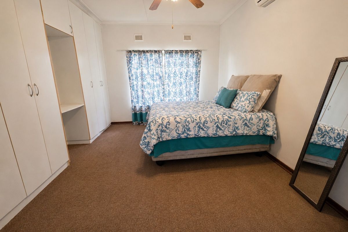 A well-proportioned bedroom featuring built-in cupboards, a ceiling fan, and a wall-mounted air conditioning unit, providing comfortable climate control.