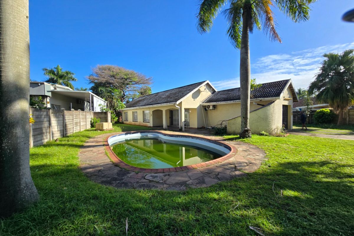 Rear exterior view of the property featuring a swimming pool with stone surround, set within a garden area with a concrete boundary wall.
