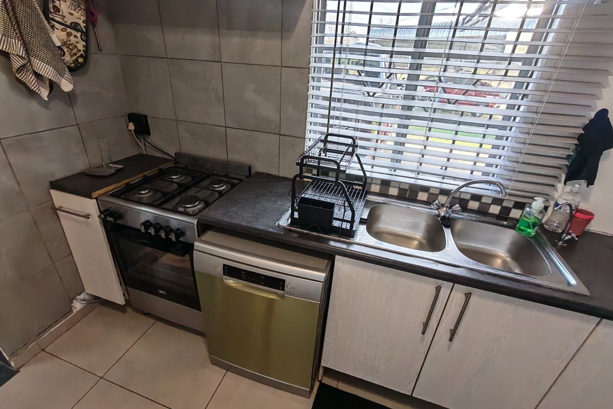 Compact kitchen featuring a gas stove, double stainless steel sink, and built-in cabinetry with tiled splashbacks and flooring.