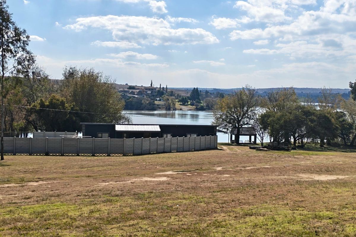 A wide-angle view of the small holding property, featuring a fenced dwelling, expansive grounds, and scenic waterfront views.