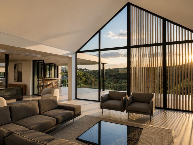 Spacious open-plan living area featuring a vaulted ceiling, exposed concrete elements, and expansive floor-to-ceiling windows with integrated timber slat screening and scenic views.