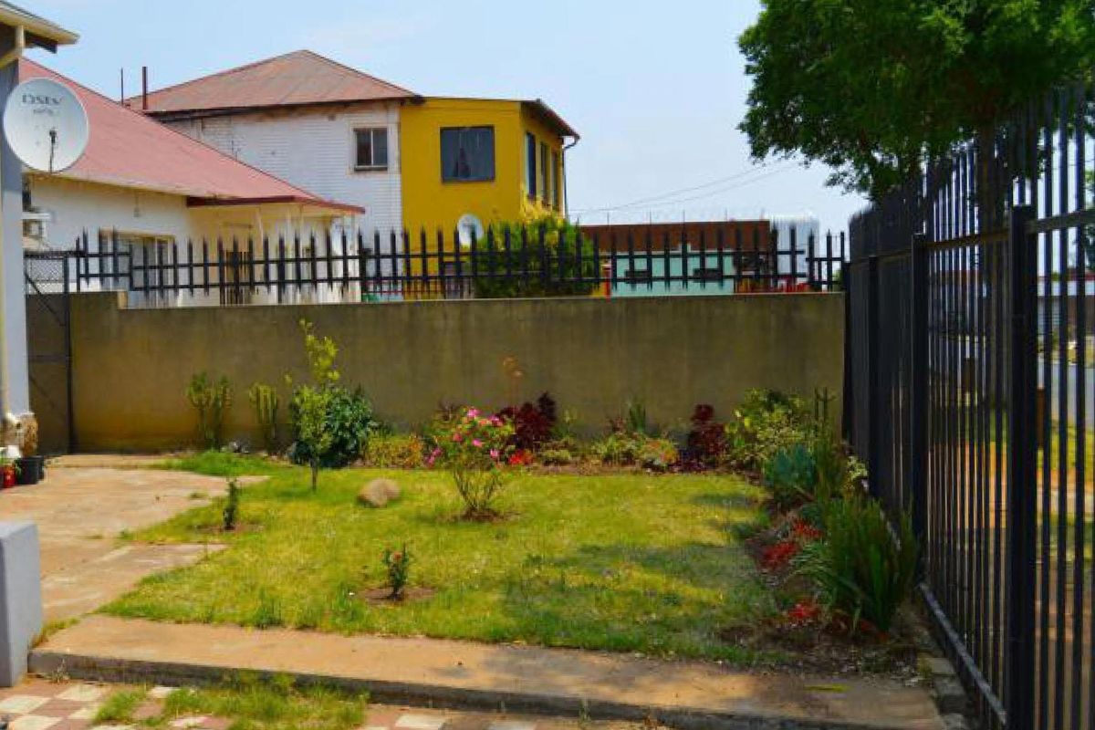 A modest rear garden area featuring a small lawn, perimeter boundary wall, and metal security fencing.