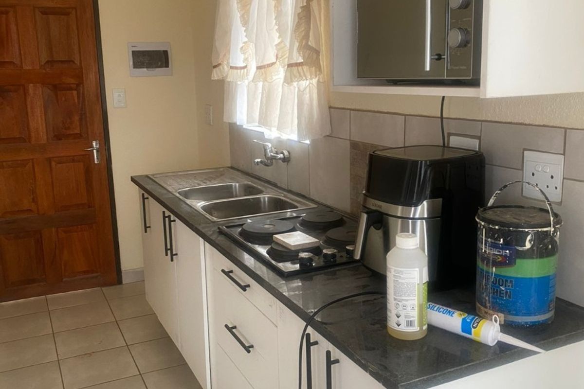 A functional kitchen featuring white cabinetry, dark countertops, a built-in hob, and a double stainless steel sink with tiled splashbacks.