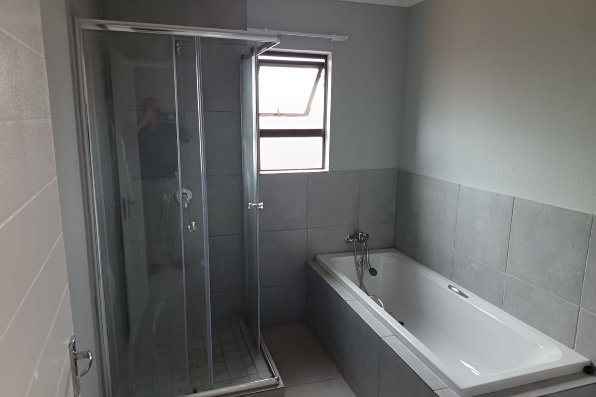 A modern bathroom featuring a glass-enclosed shower, a built-in bathtub with tiled surround, and a window for natural light.