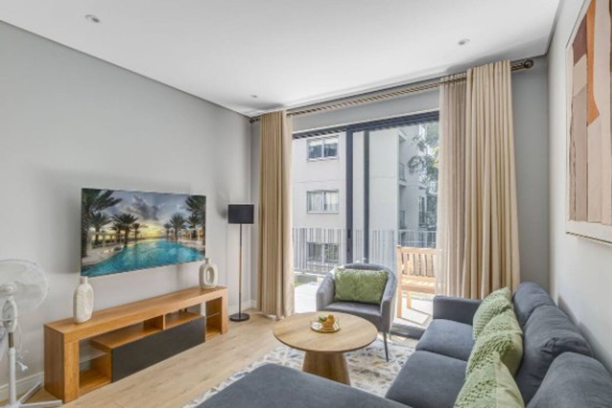 A bright living room featuring light wood-look flooring, recessed ceiling lighting, and large sliding glass doors that open onto a private balcony.