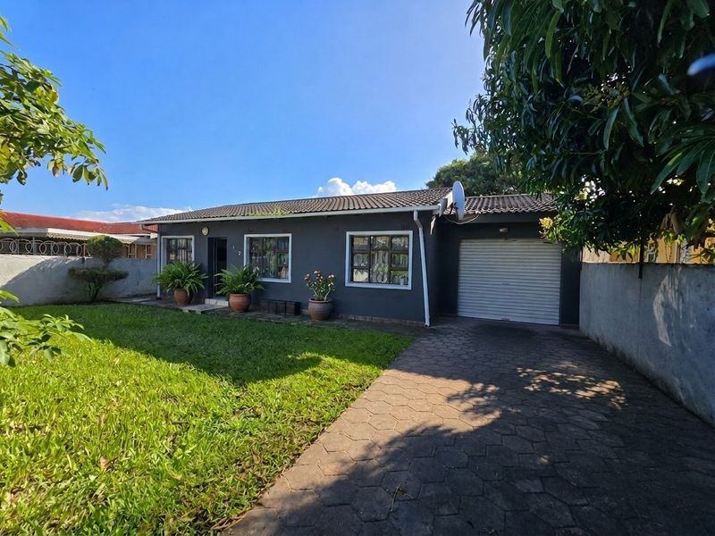 Front view of a single-story house featuring a dark grey facade, tiled roof, attached garage with a roller door, and a paved driveway.