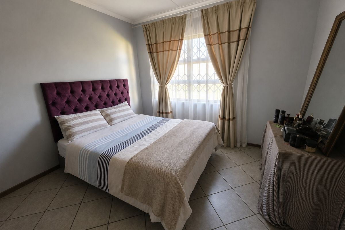 A well-maintained bedroom featuring neutral tiled flooring, a window with security bars, and neutral wall finishes.