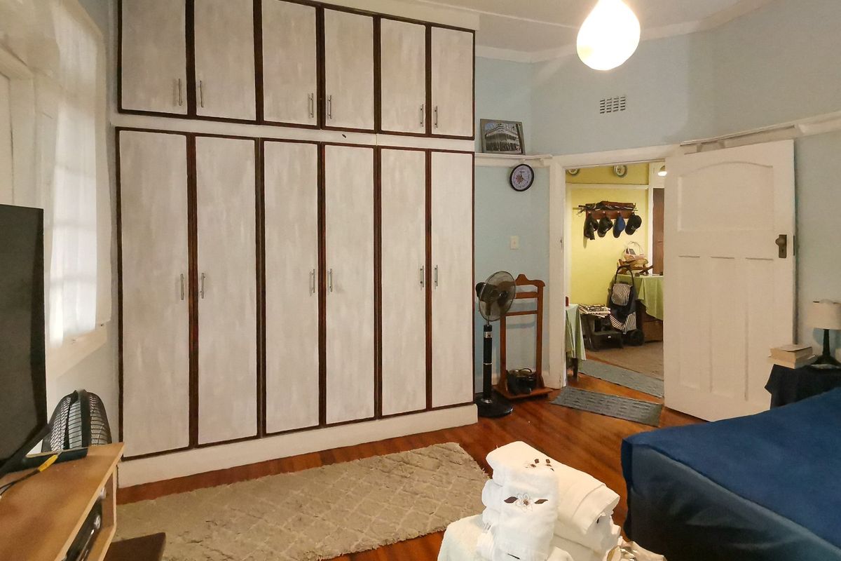 A bedroom featuring extensive floor-to-ceiling built-in cupboards, polished hardwood flooring, and a classic timber door leading to an adjacent room.
