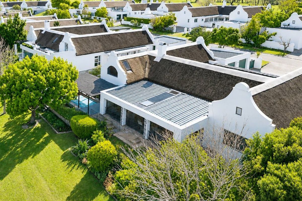 Aerial view of a residential estate featuring Cape Dutch style homes with thatched roofs, private swimming pools, and well-maintained landscaped gardens.