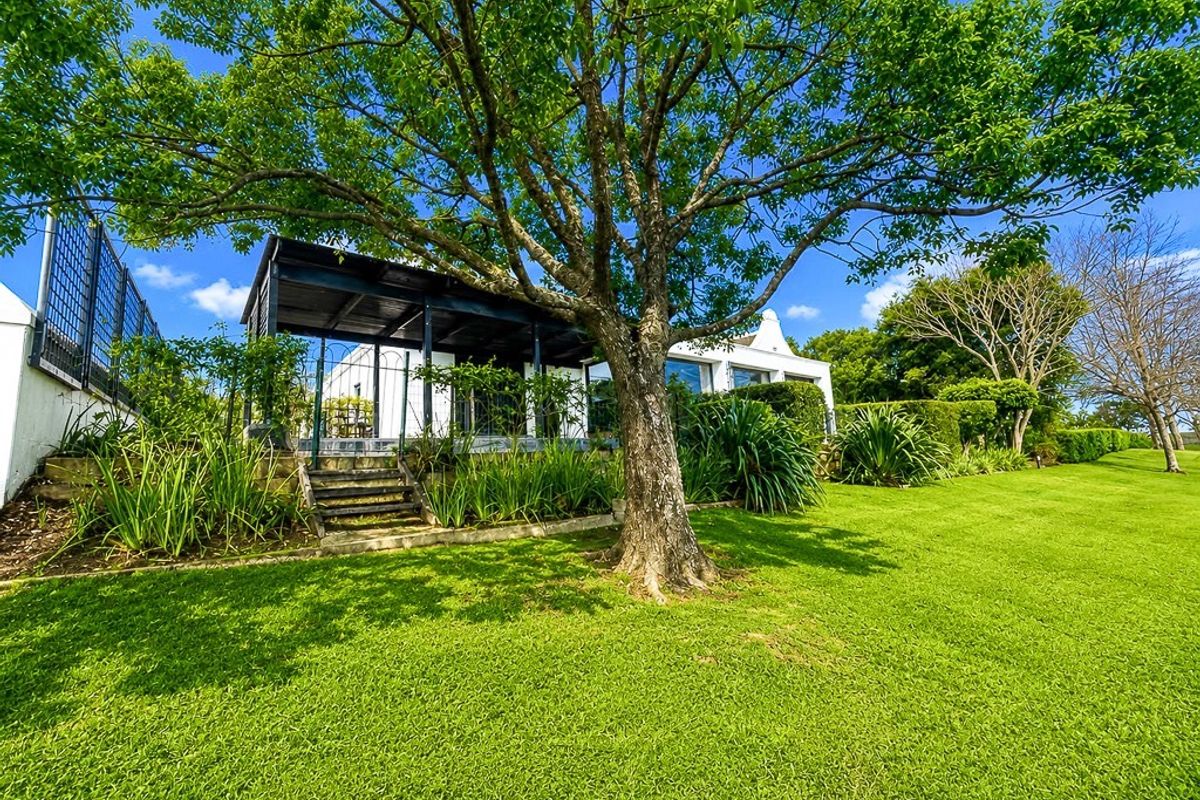 A well-maintained rear garden featuring a large mature tree, a covered patio area, and stone steps leading up to the main residence.