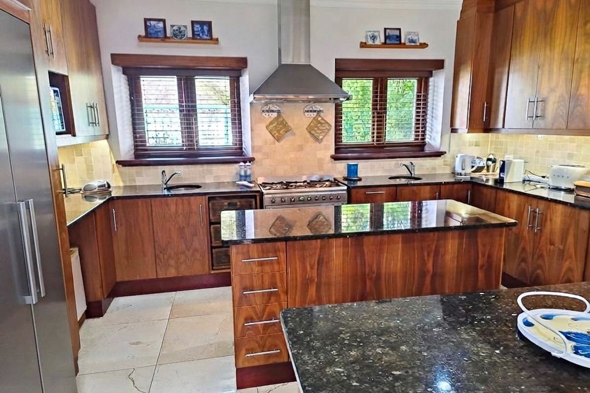 A well-appointed kitchen featuring rich wooden cabinetry, granite countertops, a central island, and high-quality stainless steel appliances including a gas hob and extractor fan.
