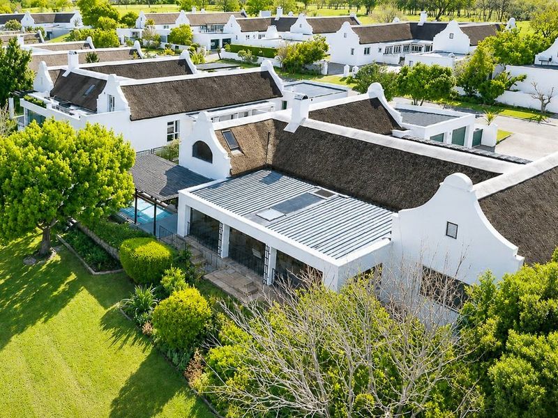 Aerial view of a residential estate featuring Cape Dutch style homes with thatched roofs, private swimming pools, and well-maintained landscaped gardens.
