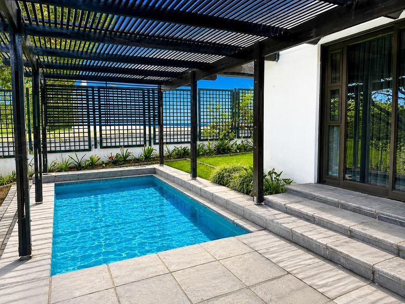 A well-maintained outdoor pool area featuring a modern timber pergola, stone patio, and direct access to the home via sliding glass doors.